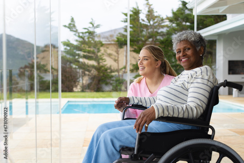 Happy caucasian female nurse and senior african american female patient in wheelchair photo
