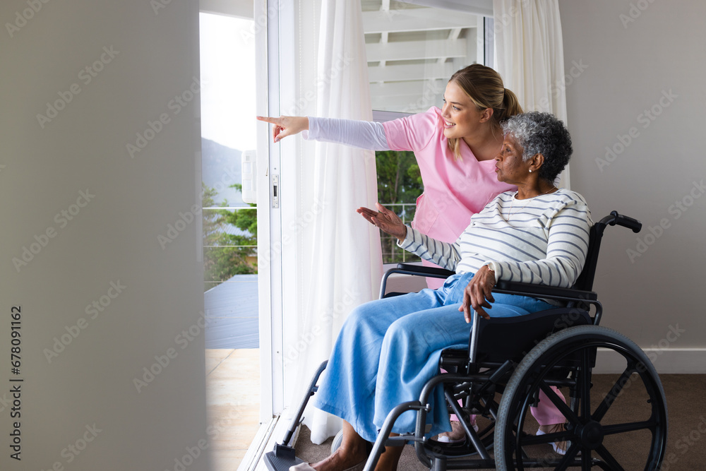 Caucasian female nurse and senior african american female patient in wheelchair by window Caucasian female nurse and senior african american female patient in wheelchair by window