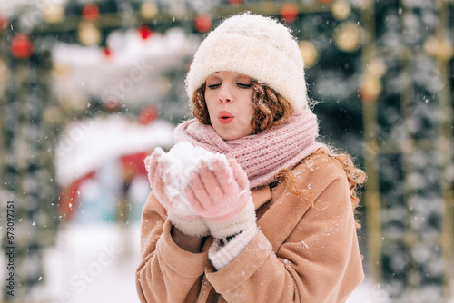 Portrait of a curly-haired girl playing in the snow. A woman blows snow on a beautiful winter day.