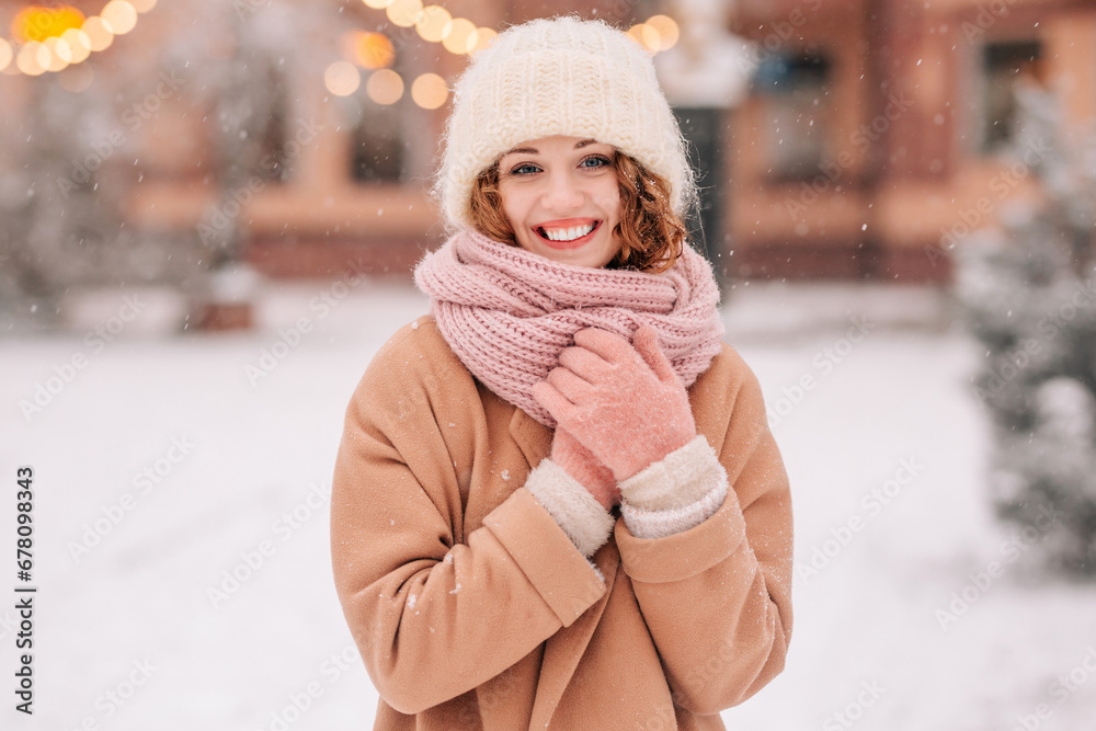 Happy girl posing in the park against the backdrop of fir trees and lights on a beautiful snowy winter day. Close shot of a woman in a cityscape.
