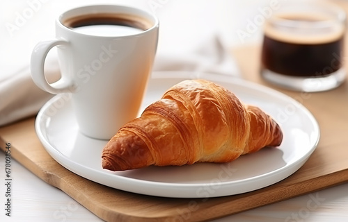 One glass cup of black coffee and croissant on white plate on white wooden table over light kitchen background
