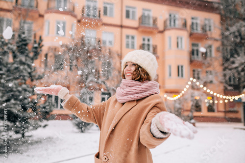 Portrait of smiling stylish middle aged woman shaking off snow from her gloves. Close shot of smiling girl playing with snow outside in the city park in winter.
