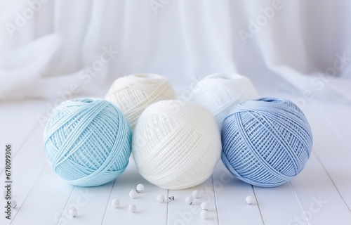 White, beige, blue balls of thread and metal knitting needles on a white wooden table soft light
