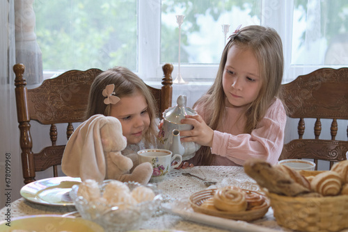 Two young sisters enjoying a vintage-style tea party indoors, pouring tea next to a window. Elements of nostalgia and childhood bonding, with a soft, natural light ambiance