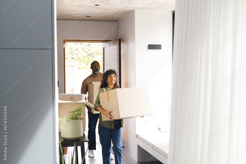 Happy diverse couple carrying packing boxes into new home, copy space Happy diverse couple carrying packing boxes into new home, copy space