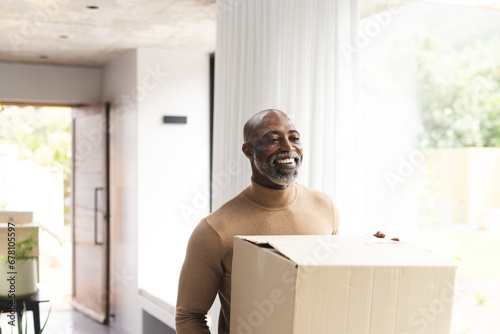 Happy african american mature man carrying packing box into new home, copy space photo