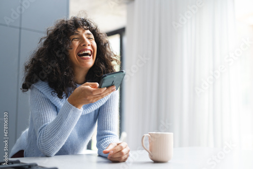 Happy mature caucasian woman talking on smartphone laughing in sunny kitchen, copy space photo