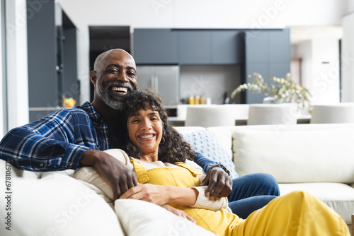 Portrait of happy diverse mature couple sitting on couch embracing in sunny living room, copy space photo