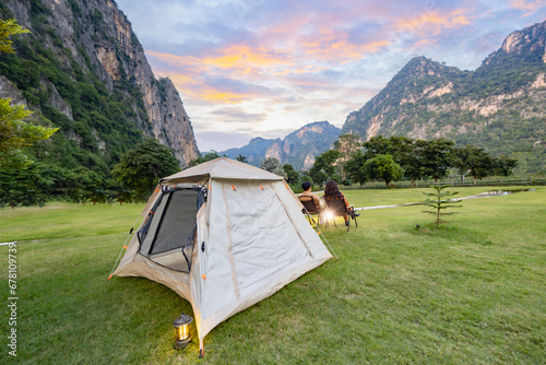 Camping and tent in nature. Adventure lifestyle of man and woman sitting in camp chairs looking at Beautiful sunset over the mountain range and enjoying view of nature. photo
