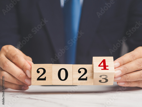Businessman holds wooden cubes with the numbers 2023 and 2024 for starting a new business plan
