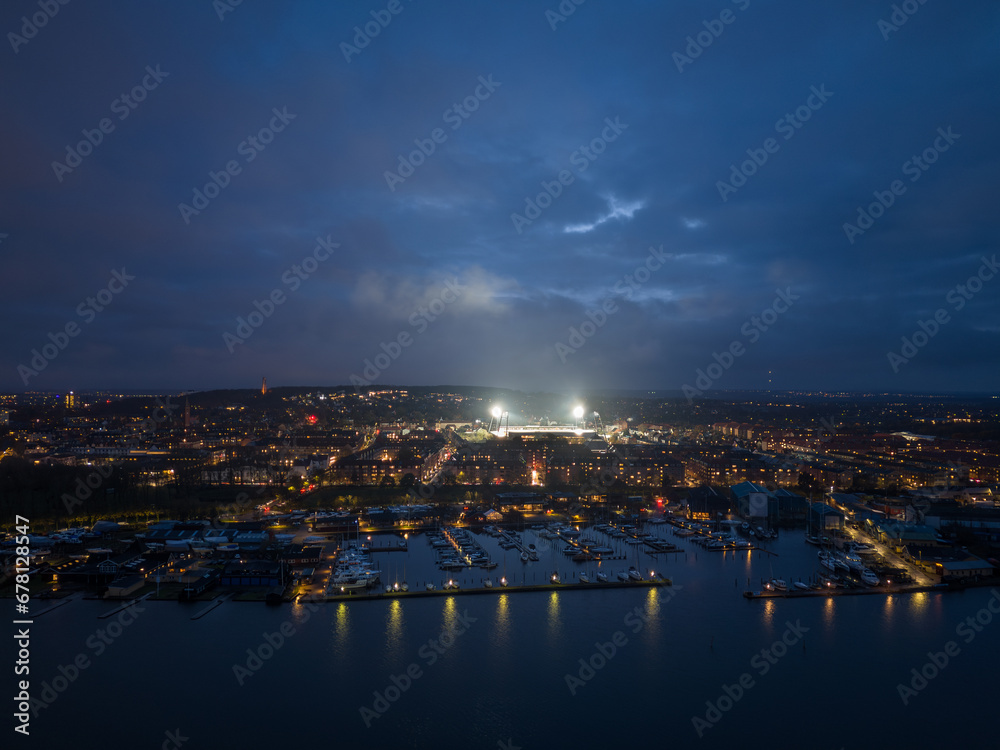 Aerial panoramic night skyline cityscape of Vestbyen city district in Aalborg during football game at the illuminated stadium. North Jutland Region, Denmark.