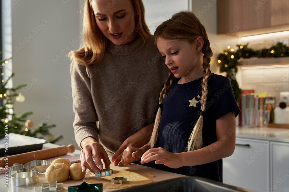 Fototapeta premium Caucasian mother and daughter making gingerbreads in domestic kitchen