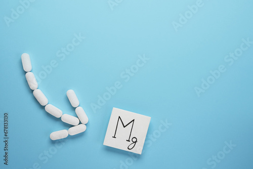 Medical pills in arrow shape with icon of  magnesium on blue background. Nutritional supplement concept. Top view, flat lay. Space for text.