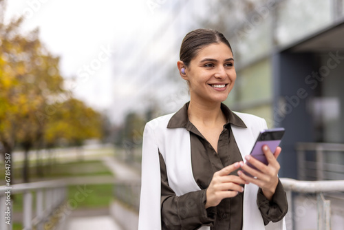 smiling young business woman using mobile phone in front of office building