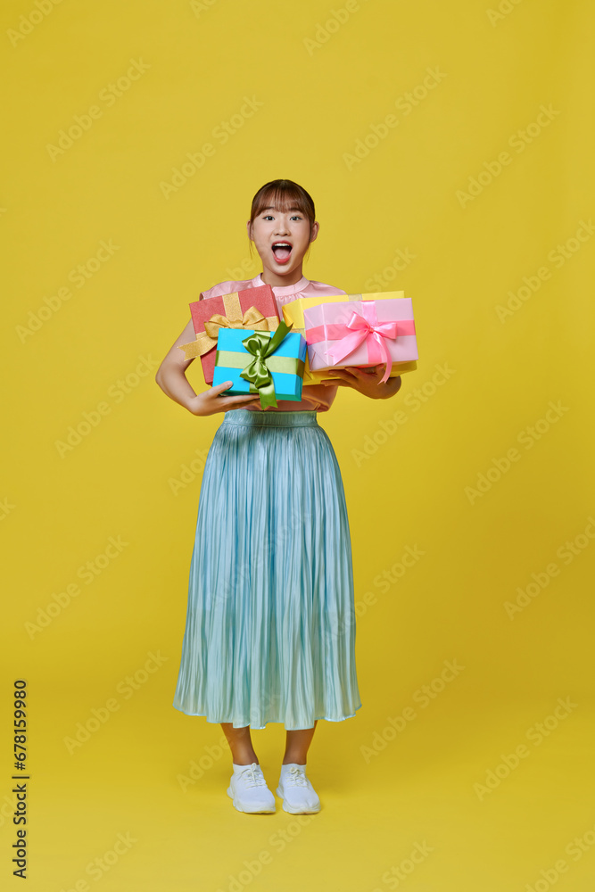 Smiling. Portrait of stylish woman emotionally posing with present boxes over yellow background Smiling. Portrait of stylish woman emotionally posing with present boxes over yellow background