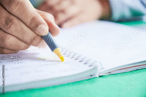 Unrecognizable woman uses a marker to highlight some words in her study notes while revising for an exam.