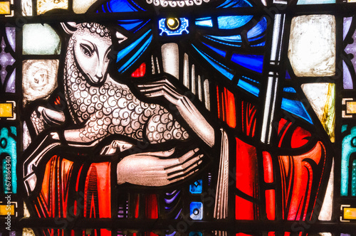 Stained glass window in a church showing Jesus holding a lamb and depicted as a shepherd