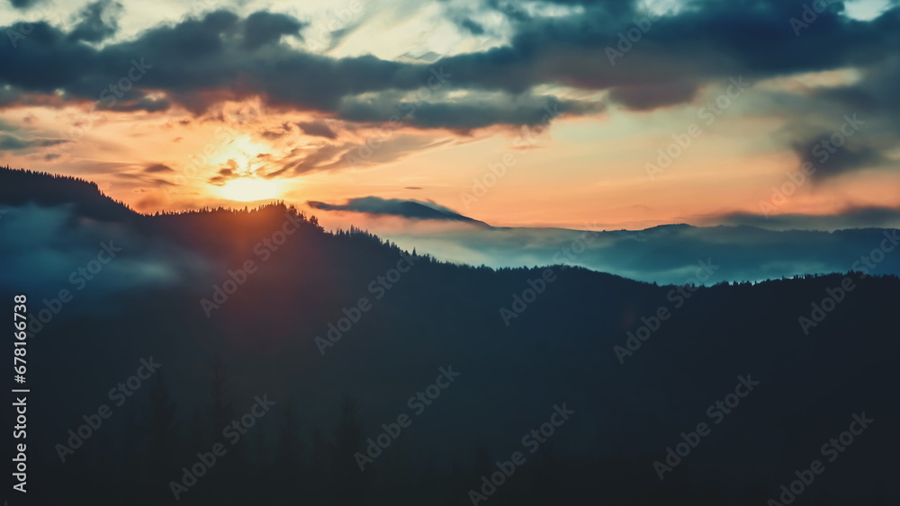 Epic foggy colorful sunrise in alp mountains. Dramatic clouds flow in bright sky, sun glow rising over mountain peak with golden light beams. Beautiful morning summer landscape.