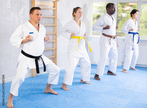 Group of multinational athletic people in kimonos try new fighting techniques at karate lessons