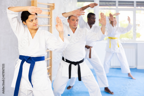 Diligent middle-aged woman attendee of karate classes practicing kata standing in row with others in sports hall