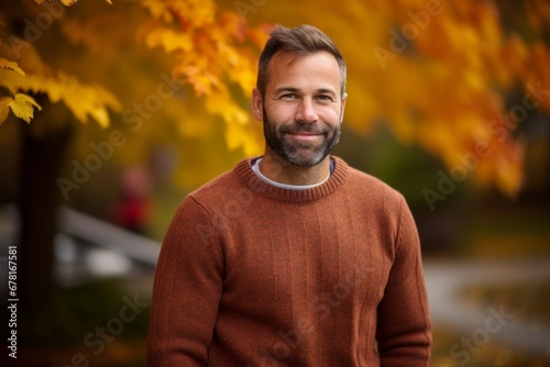 Portrait of a happy man in his 40s wearing a cozy sweater against a background of autumn leaves. AI Generation