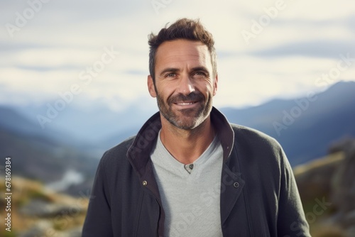 Portrait of a happy man in his 40s wearing a chic cardigan against a backdrop of mountain peaks. AI Generation