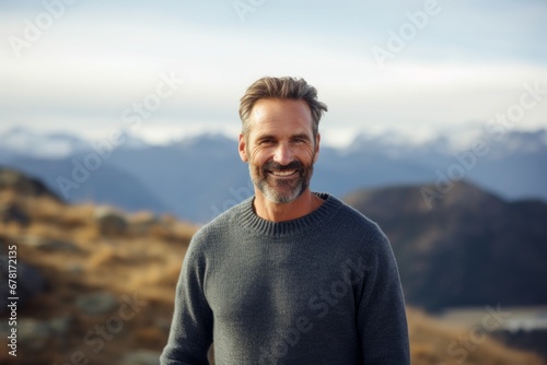 Portrait of a happy man in his 40s wearing a cozy sweater against a panoramic mountain vista. AI Generation