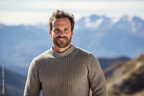 Portrait of a happy man in his 40s wearing a cozy sweater against a panoramic mountain vista. AI Generation