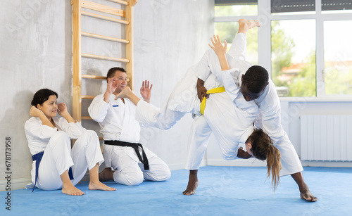 Adult man and adult woman judokas practicing judo technique in group in gym