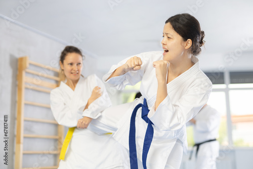 Adult woman and young woman in kimono train judo techniques in group in studio