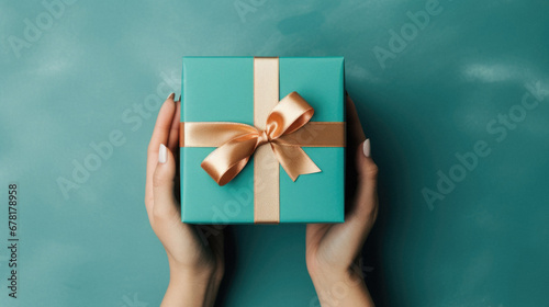 Female hands holding a gift box with a bow on a green background.