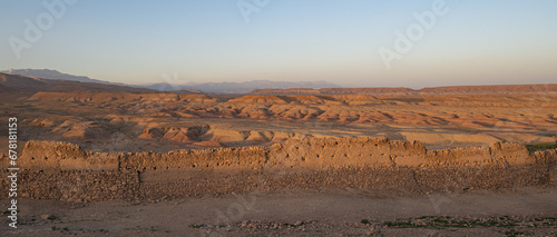 Orange stone desert hills seen in the Morocco Atlas mountains with a mud wall in front photo