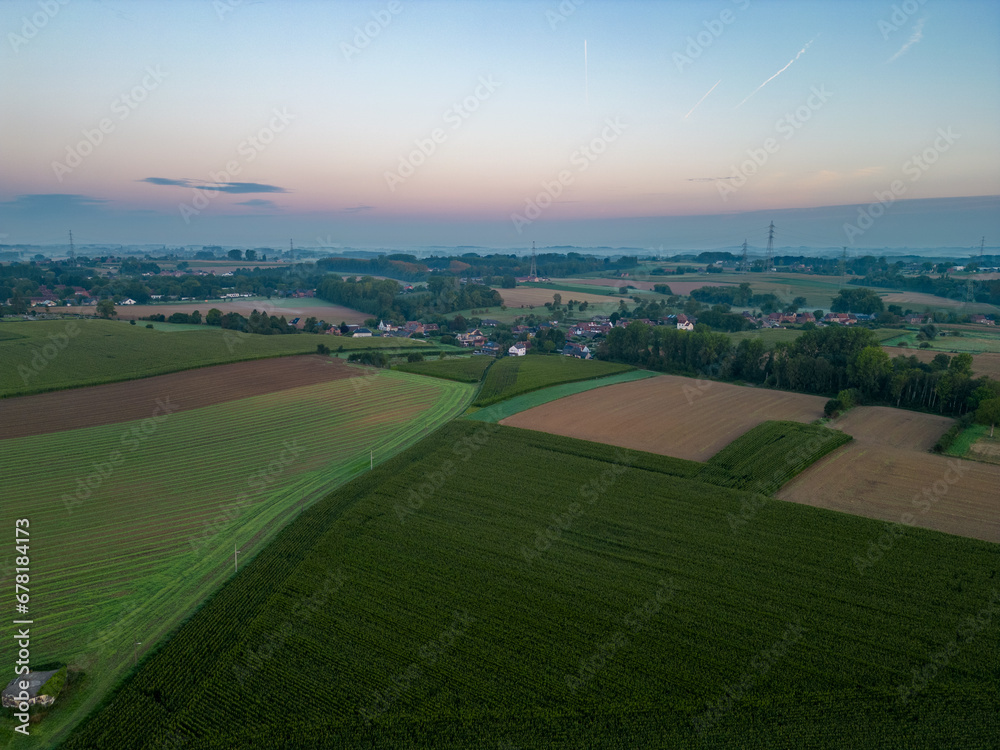 Experience the charm of the countryside with this vertical aerial panorama, showcasing a simple dirt road weaving through diverse farm fields under the captivating colors of a sunrise sky. Rural Dawn