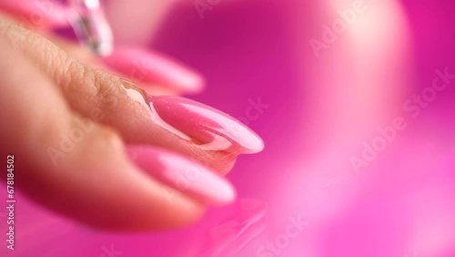 Applying cuticle oil in pipette, on fingers, manicure salon. Nail care, polish, pink shellac UV gel, varnish, manicure process in beauty salon. Over pink background. Application of nails oil closeup photo