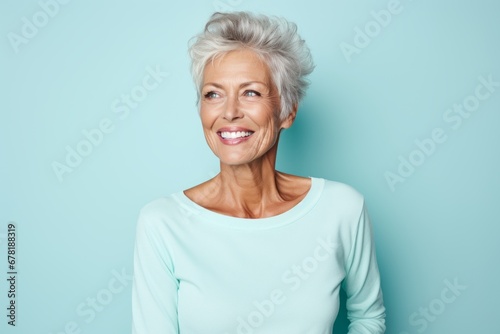 Portrait of a blissful woman in her 70s sporting a long-sleeved thermal undershirt against a pastel teal background. AI Generation