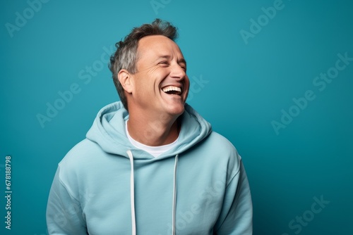Portrait of a joyful man in his 50s wearing a zip-up fleece hoodie against a soft blue background. AI Generation © CogniLens