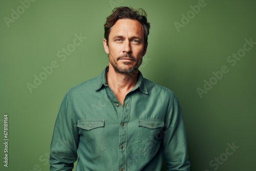 Portrait of a tender man in his 40s sporting a versatile denim shirt against a soft green background. AI Generation