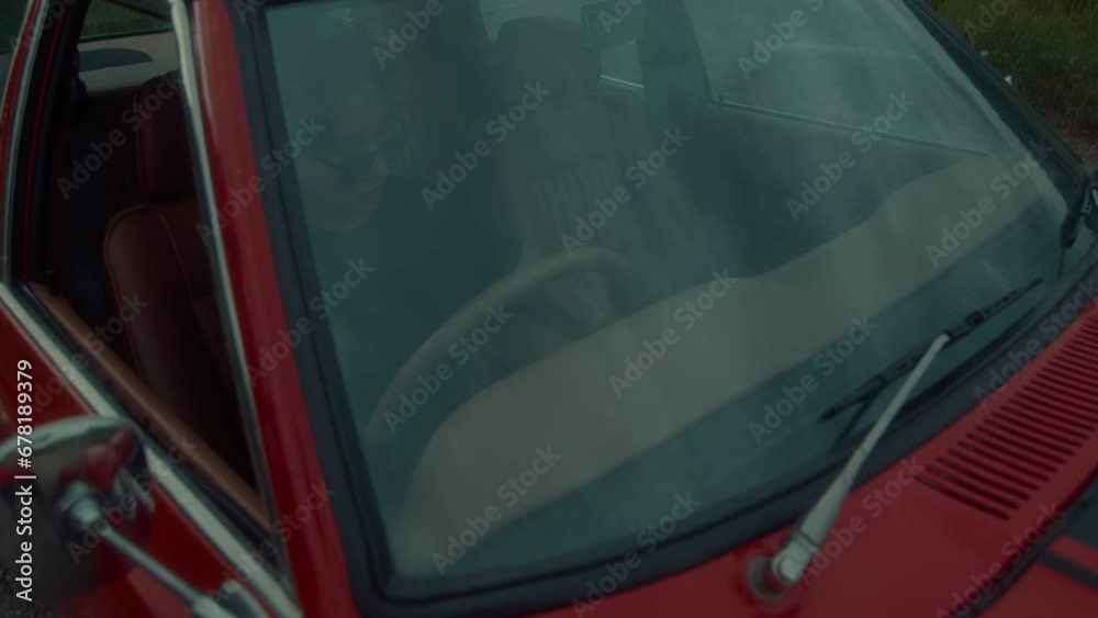 A brutal girl is sitting in a vintage red car getting ready to hit the road