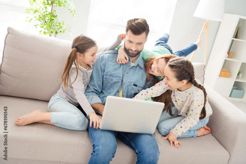 Portrait of four persons handsome guy excited funky small girls sit on sofa hand hold pull dad ear have fun indoors Portrait of four persons handsome guy excited funky small girls sit on sofa hand hold pull dad ear have fun indoors