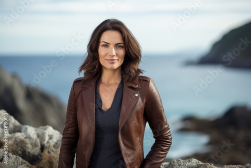 Portrait of a smiling woman in her 40s sporting a stylish leather blazer against a rocky cliff background. AI Generation © CogniLens