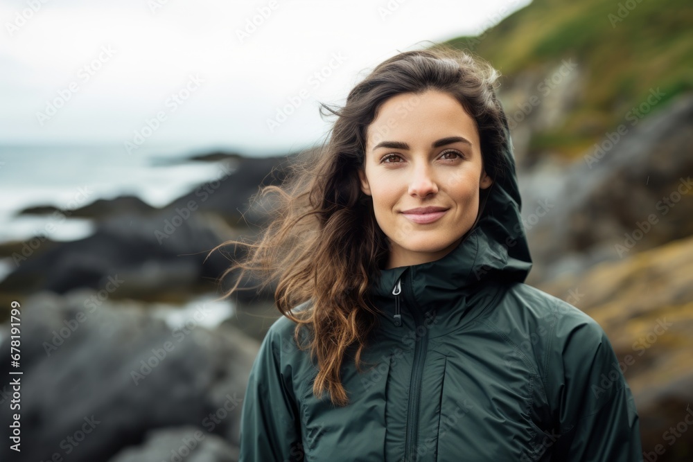 Portrait of a satisfied woman in her 30s wearing a windproof softshell against a rocky shoreline background. AI Generation