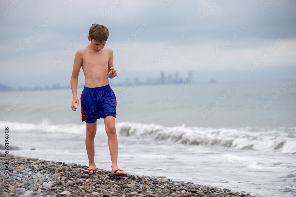 The boy walks along the rocky shore of the sea.