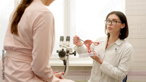 A gynecologist explains female diseases to a patient using a plastic model of the uterus and ovaries in a modern gynecological clinic. Prevention, preparation for medical examination, pregnancy. photo