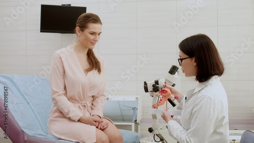 Tableau sur toile A gynecologist explains female diseases to a patient using a plastic model of the uterus and ovaries in a modern gynecological clinic