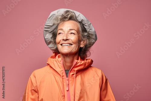 Portrait of a blissful woman in her 70s wearing a lightweight packable anorak against a solid color backdrop. AI Generation