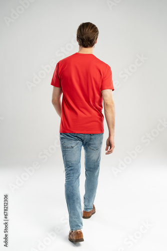Man in jeans and red t-shirt is walking. Rear view. Full length studio shot isolated on white photo