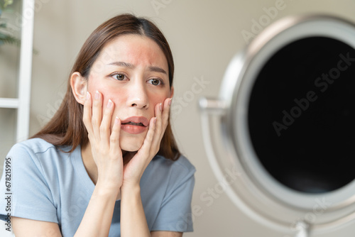 Sensitive skin with cosmetology, Asian young woman looking at red spot on her face from cosmetic allergy in the mirror.