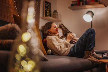 Cozy at home with tabby cat, woman with her pet on sofa ay home in evening, winter holidays concept