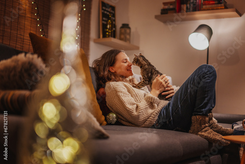 Cozy at home with tabby cat, woman with her pet on sofa ay home in evening, winter holidays concept © olezzo