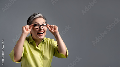 surprised 50s elderly woman looking through glasses on green friday sales on grey background photo
